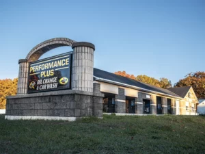 Large sign with Performance Plus logo in front of large building with multiple car wash and oil change bays.